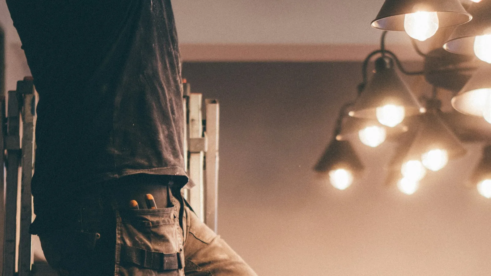 Electrician climbing a ladder while installing lights at a customer property